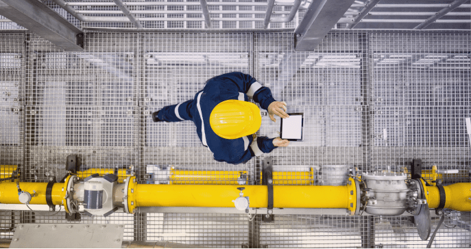 Man walking in a warehouse with a yellow hard hat on while scrolling on a tablet - Applied CAx Siemens software partner USA