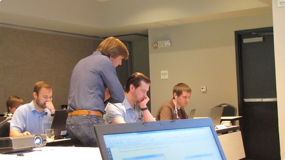 Group of people in a classroom with the instructor helping one student with computer work - Applied CAx Siemens software partner USA femap training