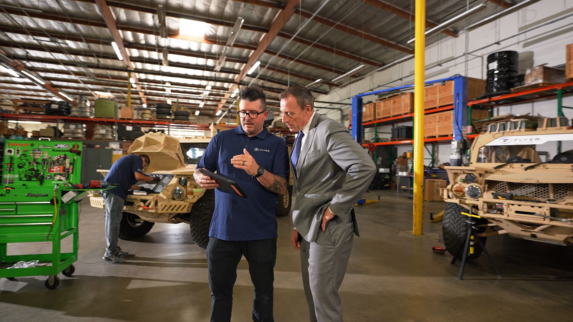Two men from flyer defense looking at a tablet in a warehouse - Applied CAx Siemens software