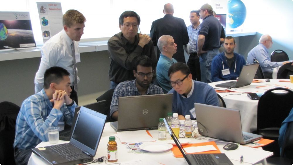 Group of mean gathered around a computer in a conference room - Applied CAx Siemens software partner USA